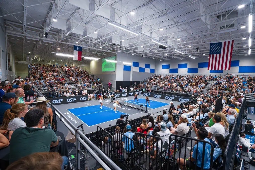 Indoor pickleball match with players and large audience.