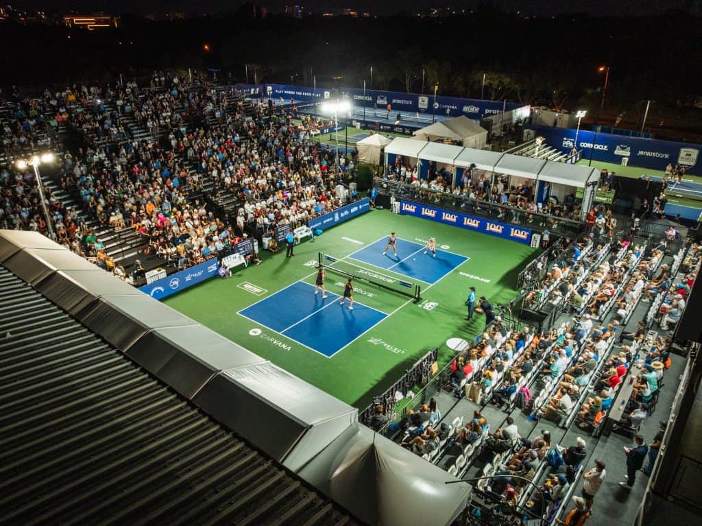Crowd watching Major League Pickleball match at night with bright court lights.